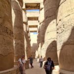 Four young travelers walking together past massive ancient columns at a historic temple in Luxor, using a curated Egypt travel guide to unlock bucket-list experiences.